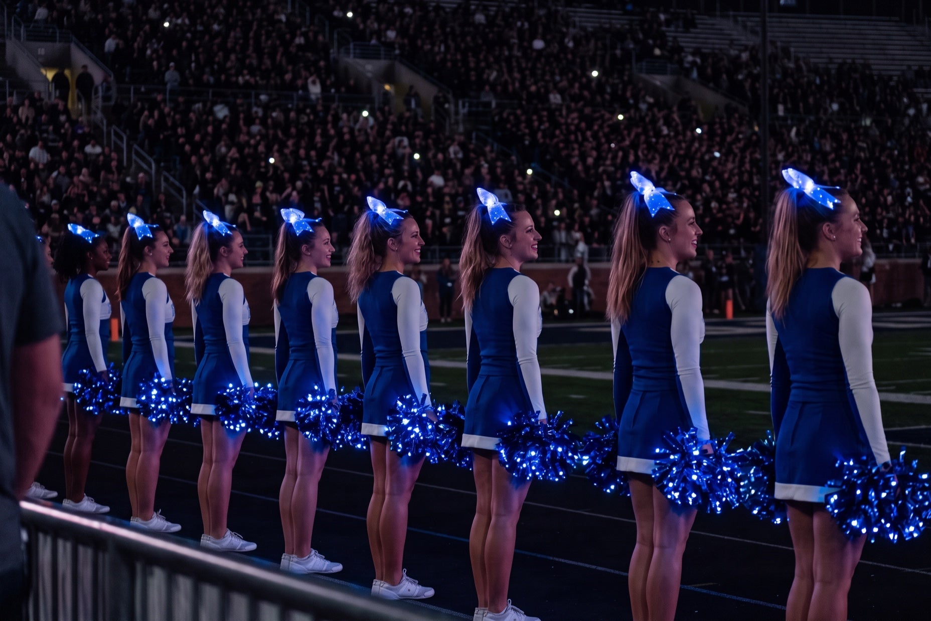 Cheer camp vs clinic: squad in royal blue with blue light-up bows on high ponytails and blue LED pom poms at a night game