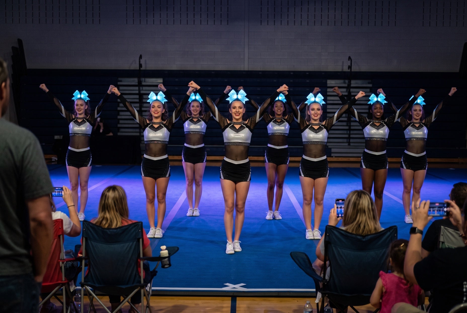 Light up LED cheer bows glowing ice blue on an all-star team at a lights-down gym showcase