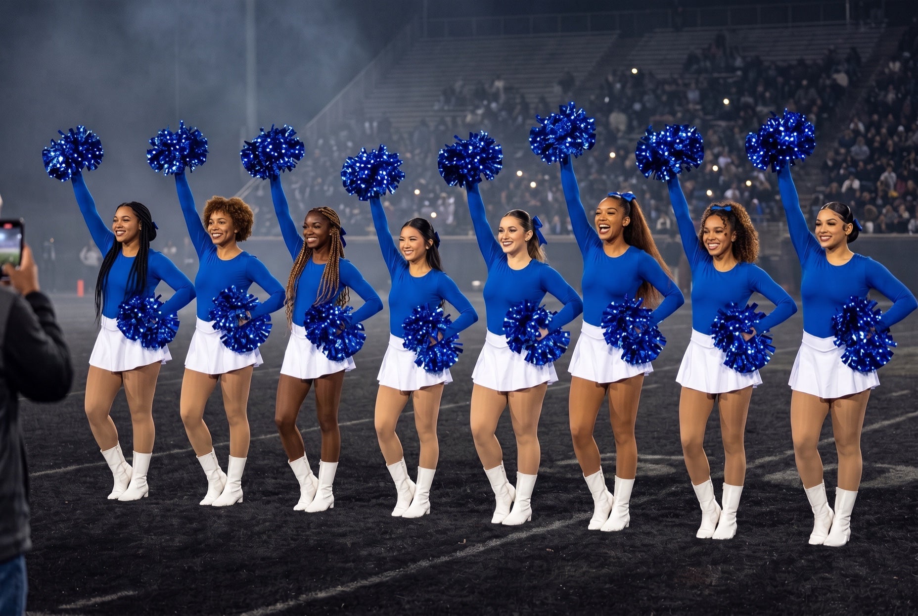 Drill team line of eight in royal blue and white with royal blue LED pom poms on a dark stadium field at halftime