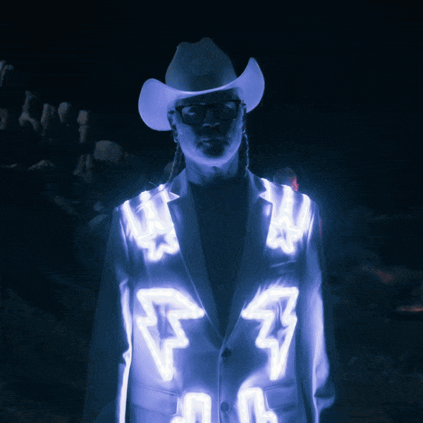 Person wearing white glowing LED nudie suit jacket with cowboy hat against dark background ideal for country music concerts rodeo events and western-themed nightlife parties