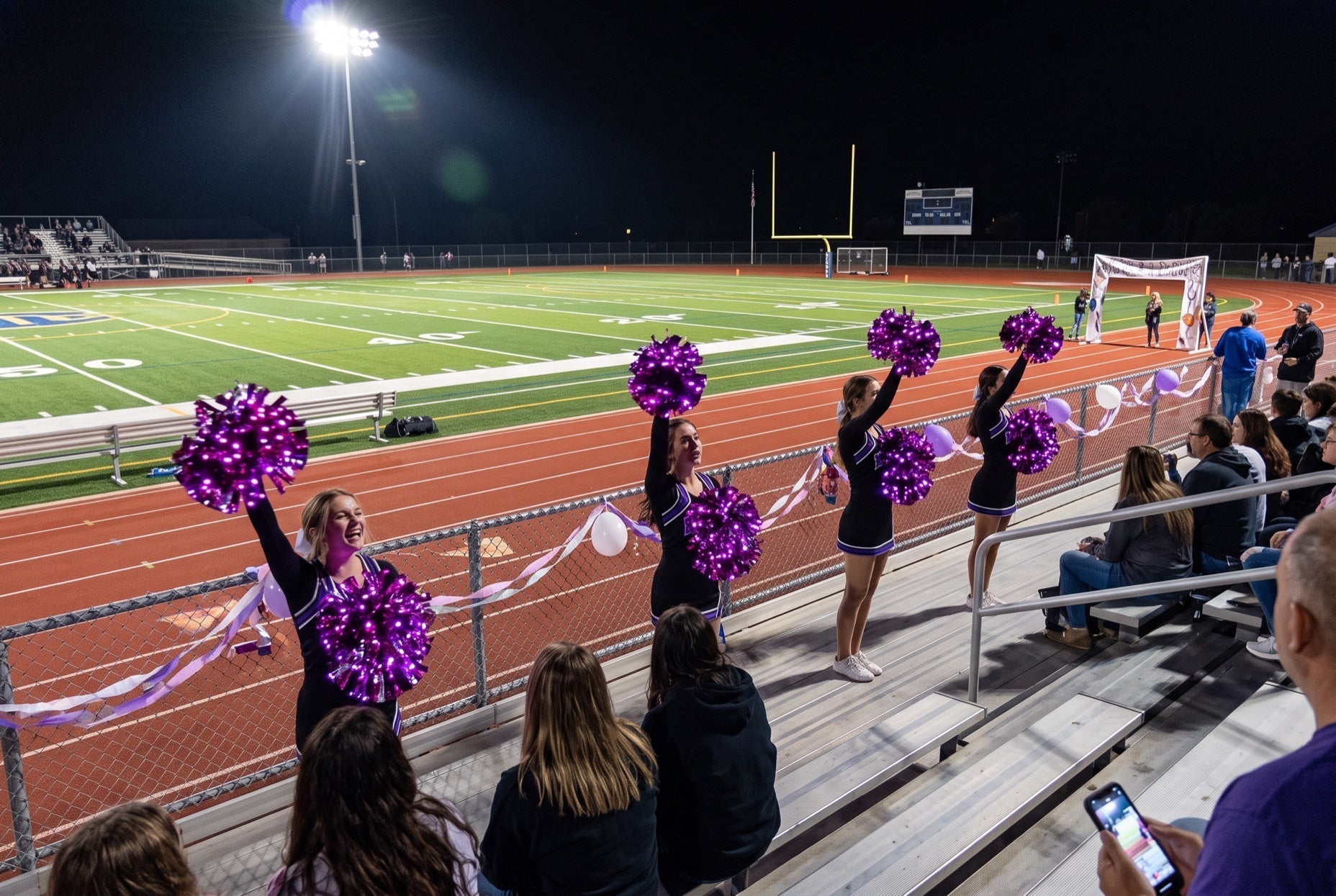Light up LED pom poms glowing purple at a homecoming football game at night