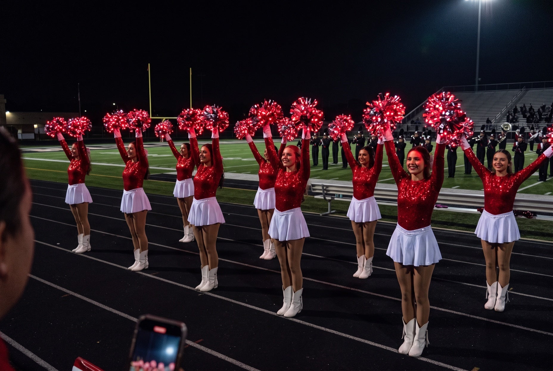Light up LED red pom poms glowing on a Texas high school drill team in red sequins and white boots at a night game
