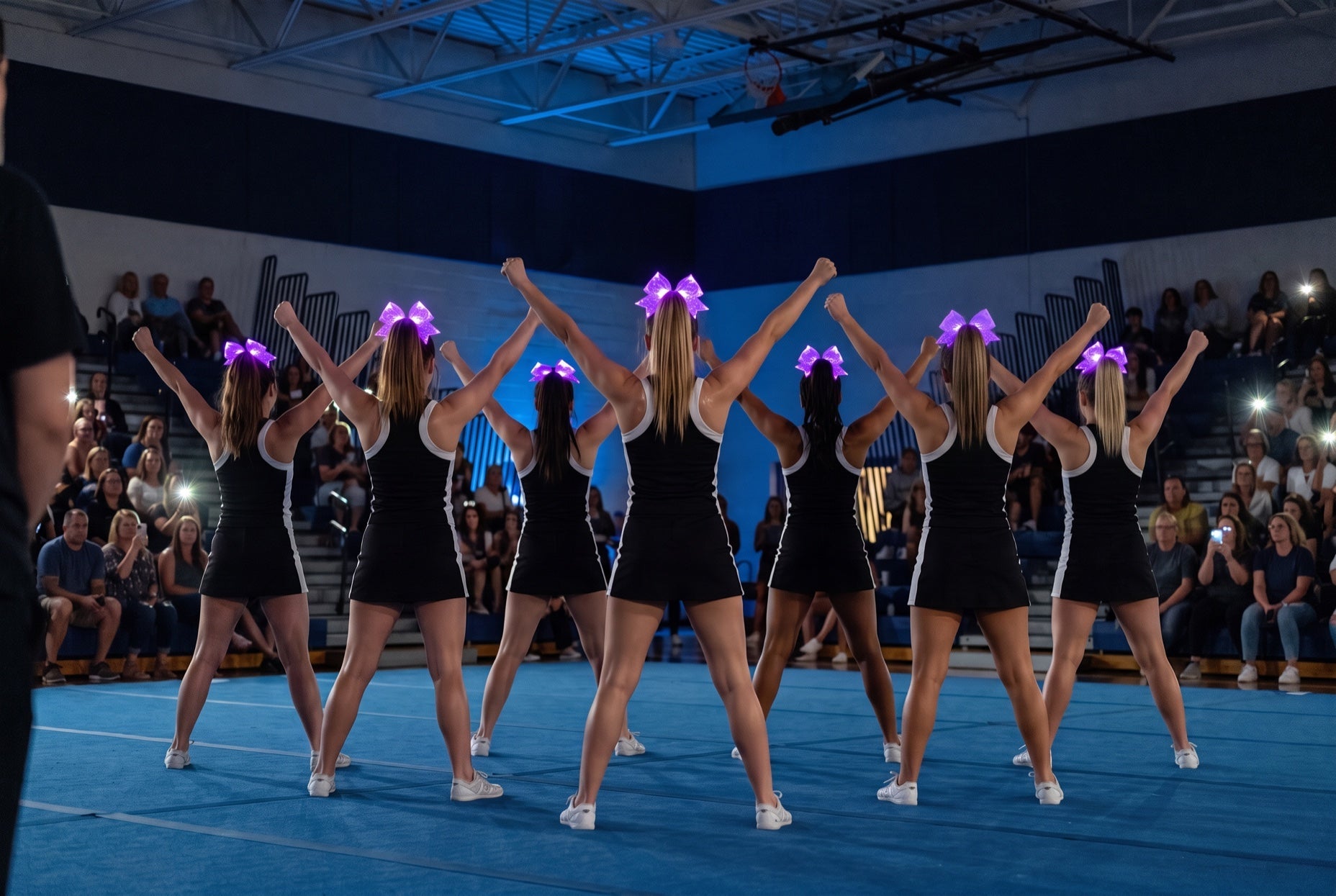 What to wear to cheer tryouts: squad in black and white with purple light-up bows on high ponytails at a showcase