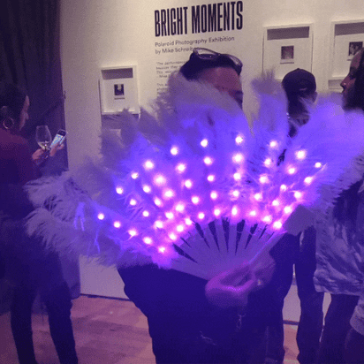 Person with blue LED feathered fan at indoor event - Illuminated remote-controlled feather accessory for nightclubs, cosplay conventions, dance performances, and fashion shows