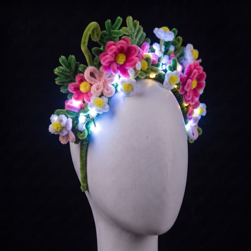 Floral pipe cleaner headband by Neon Cowboys on a white mannequin, a crown of handmade pink and white daisies and green fern leaves glowing with cool white LED fairy lights (included, you add them yourself), a light-up flower crown for festivals, raves, fairy and Halloween costumes