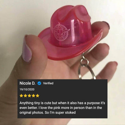 Hand holding pink cowboy hat bottle opener keychain with customer review showing 5-star rating for festival accessories