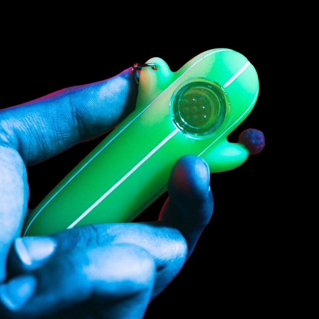 Person holding green glow-in-the-dark cactus silicone pipe with glass bowl for music festival camping outdoor adventures and late-night gatherings that provides both function and unique glowing style