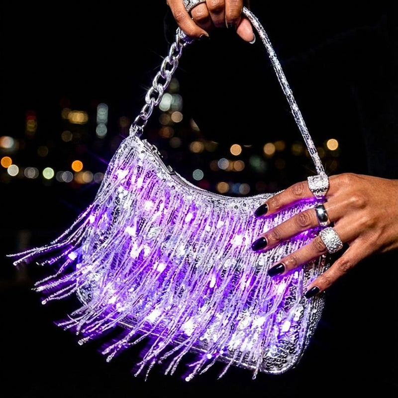 Hand holding a silver LED fringe purse glowing purple against a city skyline at night, a light up purse and light up fanny pack alternative, glowing star purse and clear-bag concert bag perfect for raves, EDM concerts, festivals and nights out, Neon Cowboys