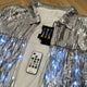 Silver LED sequin fringe jacket laid flat with accessories - Complete package contents showing jacket, remote control, and batteries for color-changing illuminated apparel
