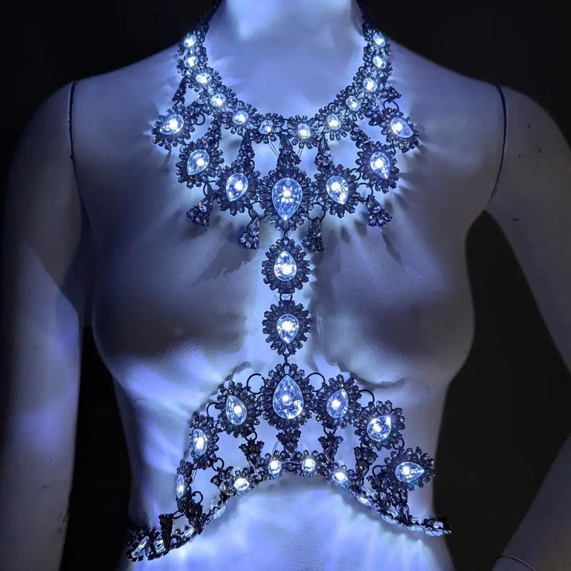 Neon Cowboys multicolor LED rhinestone body chain on a mannequin, a crystal teardrop harness glowing bright white, illuminated crystal light up body chain stagewear for go-go dancers, burlesque performers and showgirls at raves, EDM festivals and Cleopatra-inspired costumes, Neon Cowboys