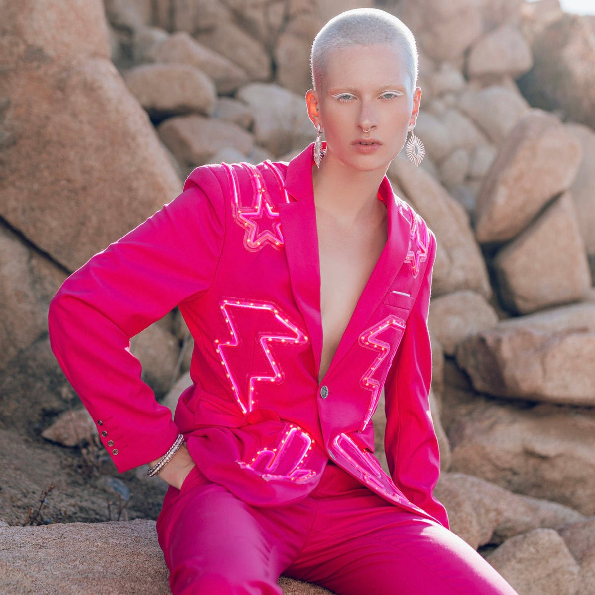 Woman in hot pink light up nudie suit jacket against rock formation perfect for desert music festivals Burning Man outfits and fashion editorial photoshoots