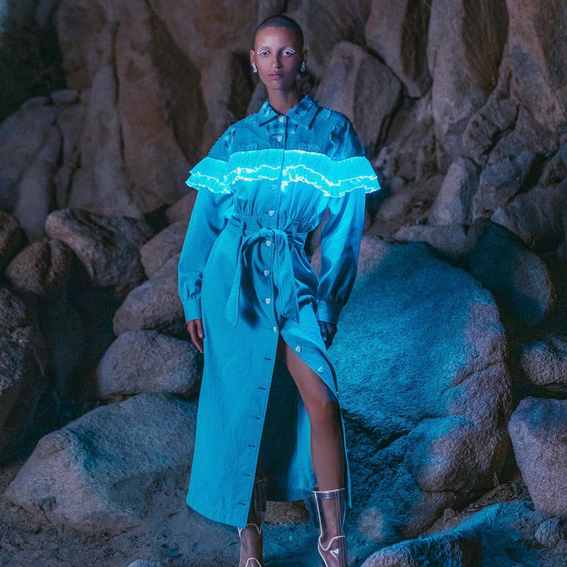 Model in a Neon Cowboys light up ruffle denim dress with glowing teal ruffle trim on desert rocks, led festival stagewear for showgirls and disco cowgirls, perfect for country music festivals, western themed parties and rodeo events, Neon Cowboys