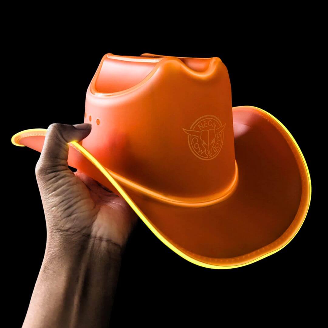 Orange sustainable plastic LED cowboy hat held in hand - Color-transition illuminated western headwear in vibrant colors for summer festivals, beach parties, country bars, and western fashion statements