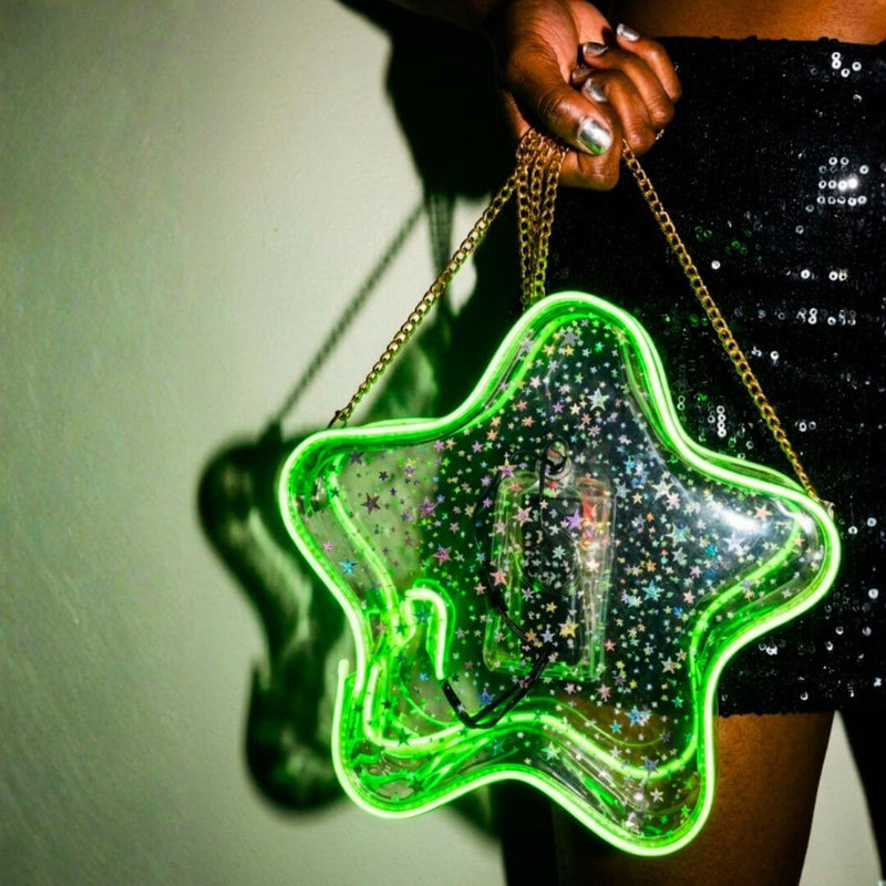 Woman in a black sequin skirt holding a green glowing LED light up star crossbody bag with a gold chain, star purse and clear bag concert accessory for music festivals, EDM raves, and stadium concerts with a clear bag policy, Neon Cowboys