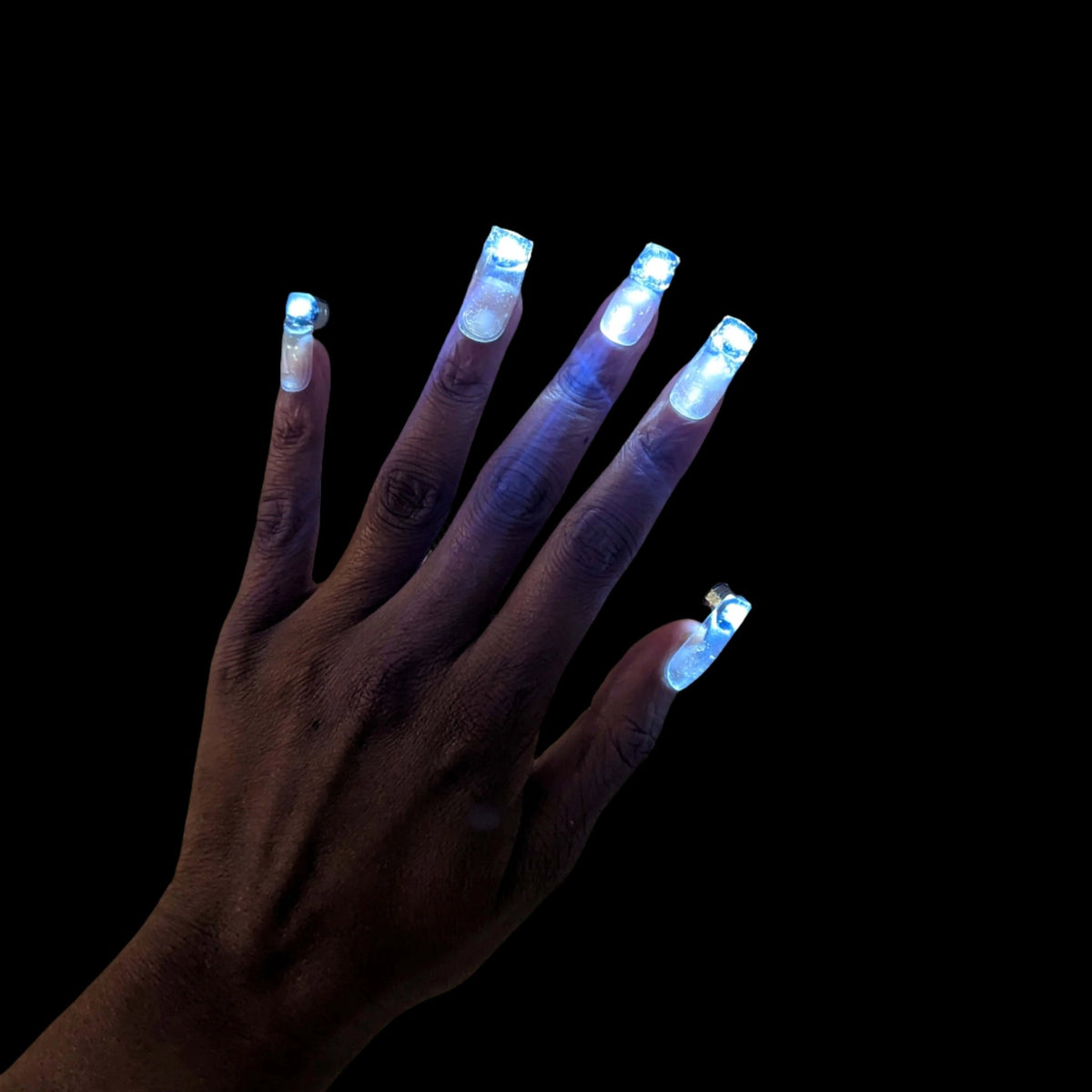 Hand with glowing blue LED press-on nails in dark setting - Illuminated false nails for festivals, concerts, cosplay events, and viral TikTok manicure trends