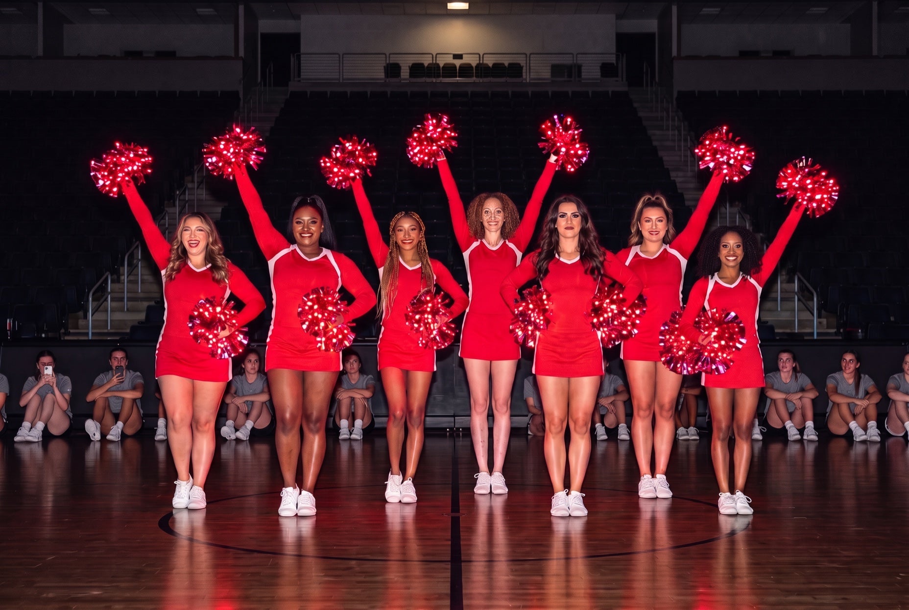 Cheer and dance costs: seven cheerleaders in red raise red LED pom poms at center court as adult attendees watch