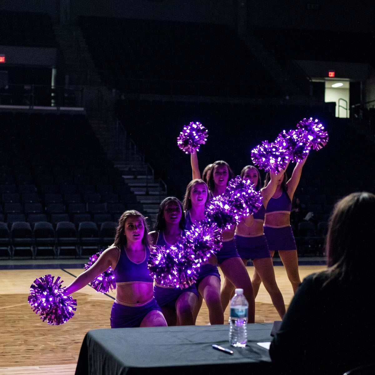 Dance team poms in competition: a pom squad performs a ripple with purple light-up pom poms, seen from the judges' table