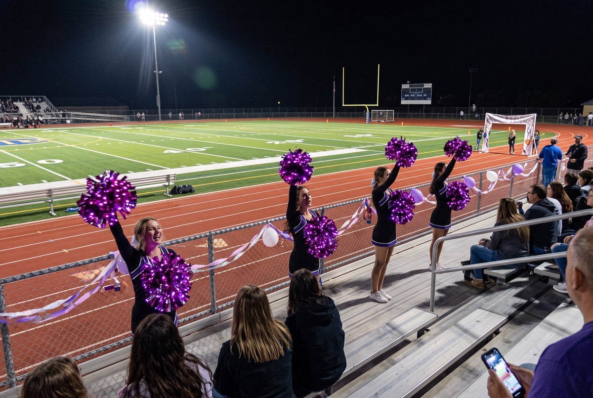 Light up LED pom poms glowing purple at a homecoming football game at night