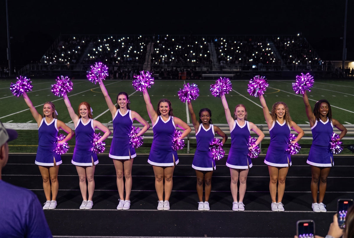 Cheer clinic fundraiser night: college squad in purple raises purple LED pom poms on a dark stadium track at halftime