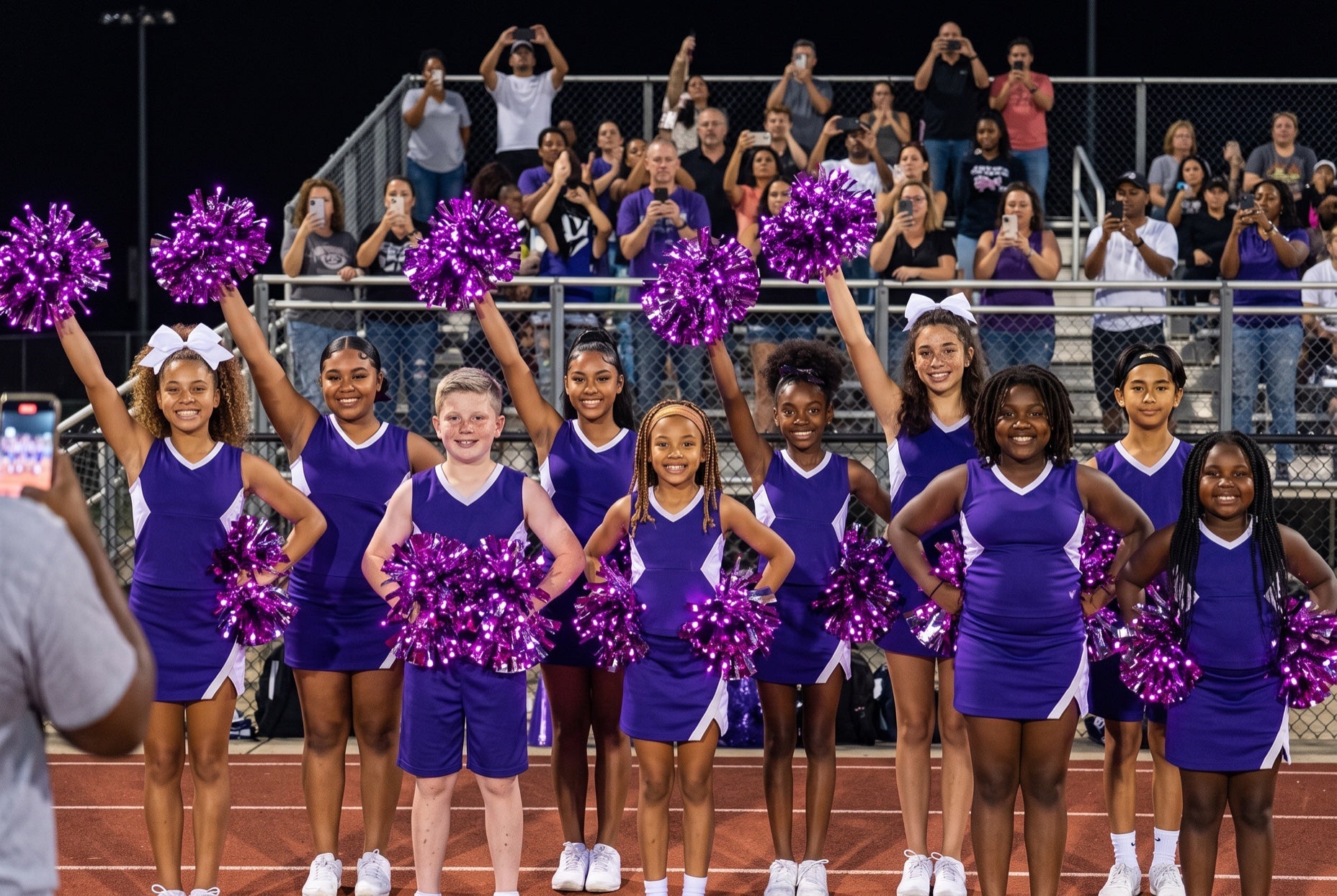 Light up LED purple pom poms glowing on a youth rec cheer team at a night youth football game