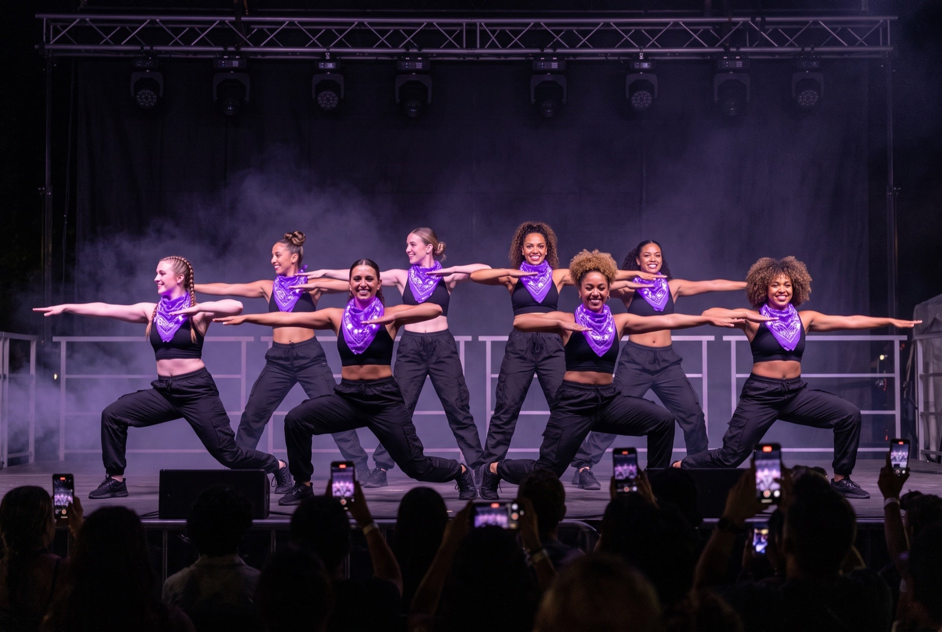 Light up bandanas in purple on an eight-dancer team lunging in unison on an outdoor festival stage at night