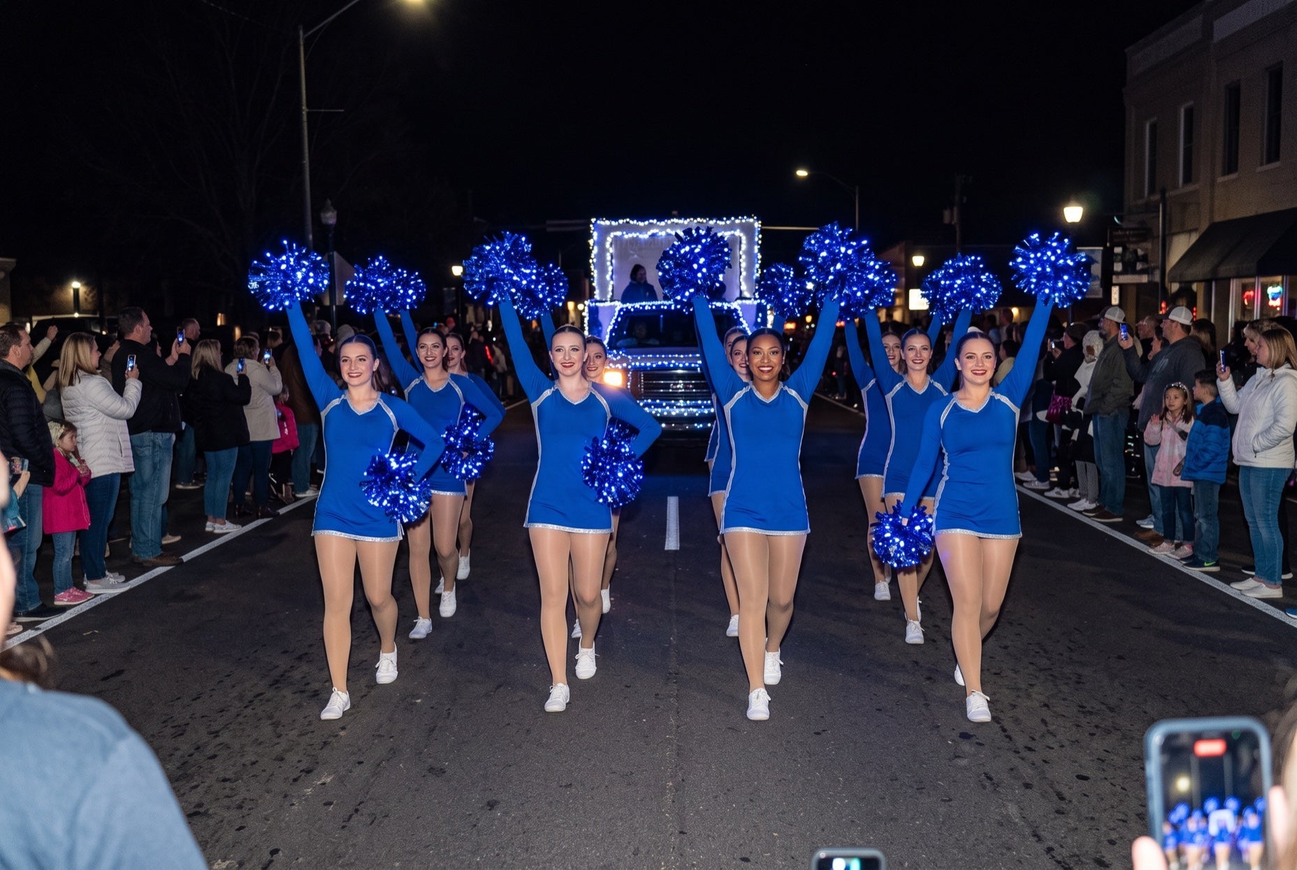 High school dance team marching with glowing blue LED light-up pom poms in a night Christmas parade of lights