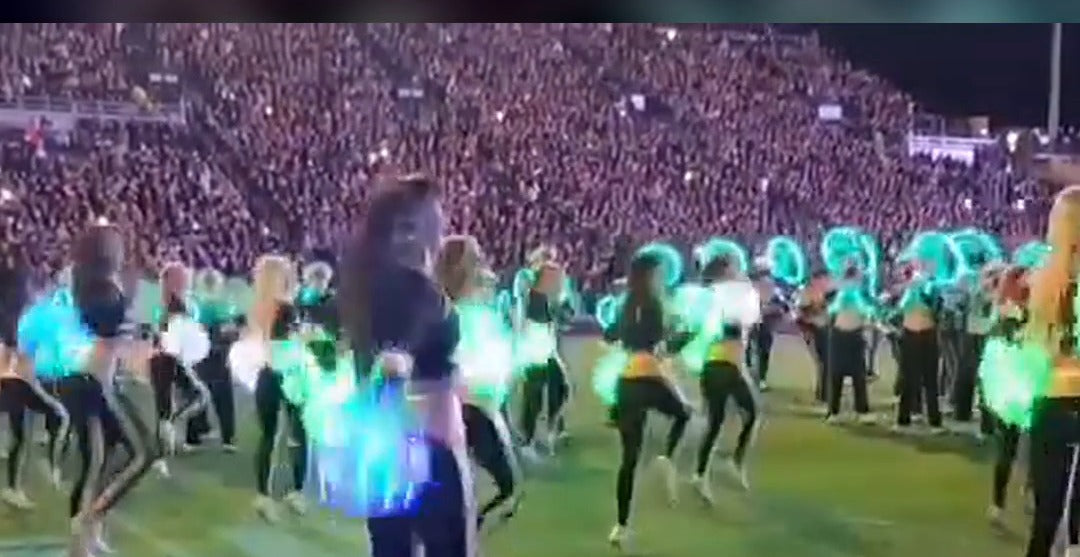 Purdue Goldusters dancing with glowing LED pom poms in front of the All-American Marching Band at night
