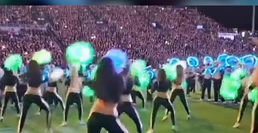 Purdue Golduster Dance Team with LED light up pom poms glowing green, blue and purple on the field at a night game