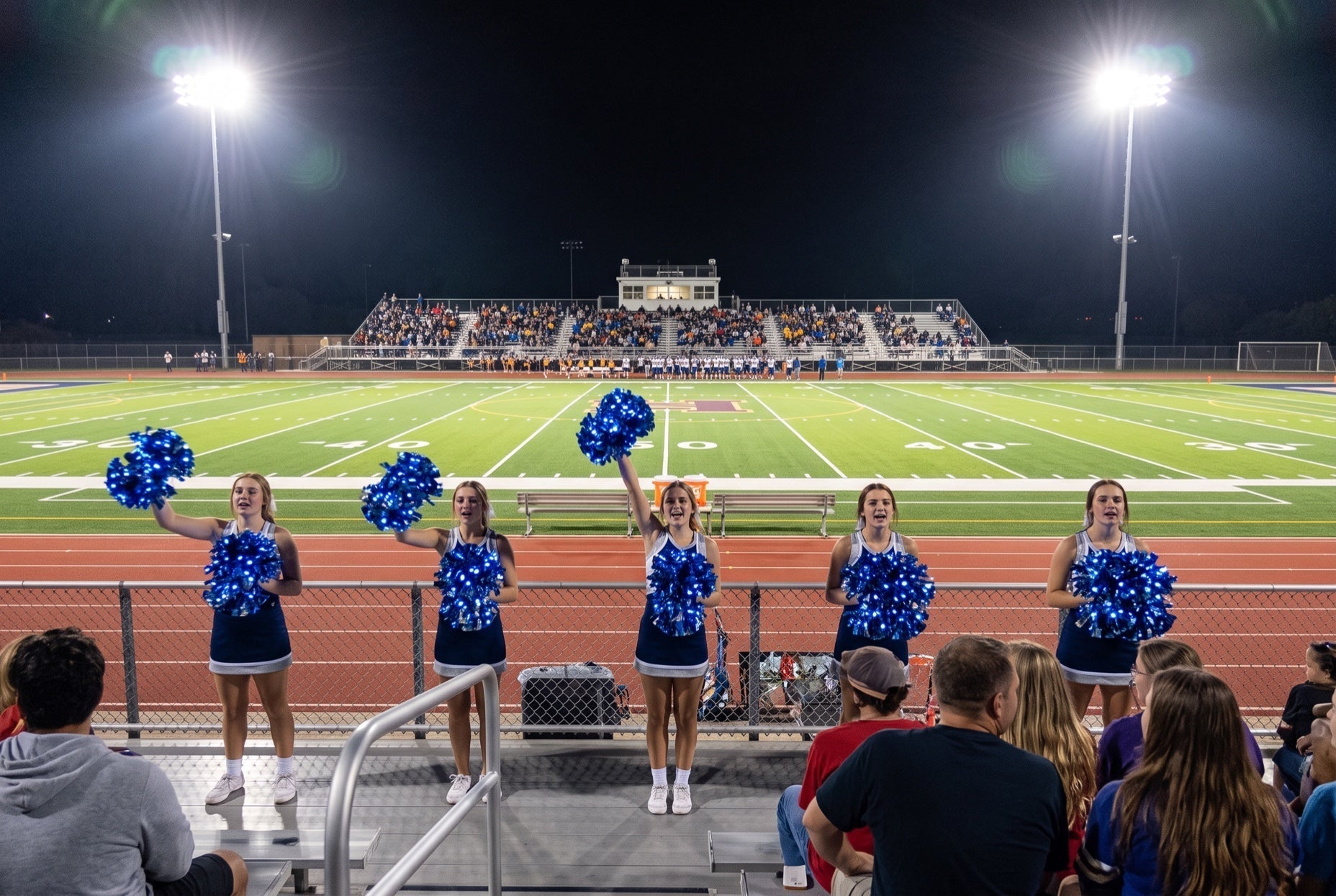 Light up LED pom poms glowing blue under stadium floodlights at a night football game