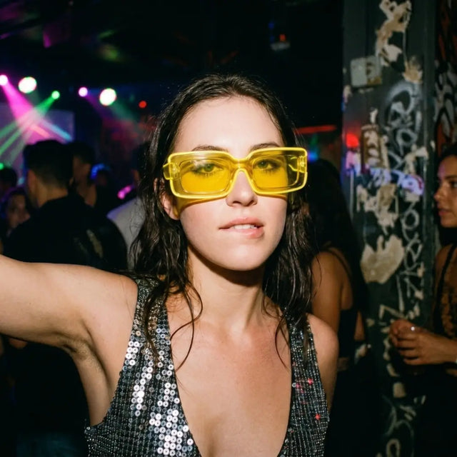 Woman at a nightclub wearing yellow tinted LED light up party sunglasses over a sequin top, glowing cyberpunk led glasses and festival sunglasses for raves, EDM concerts, and glow parties, Neon Cowboys