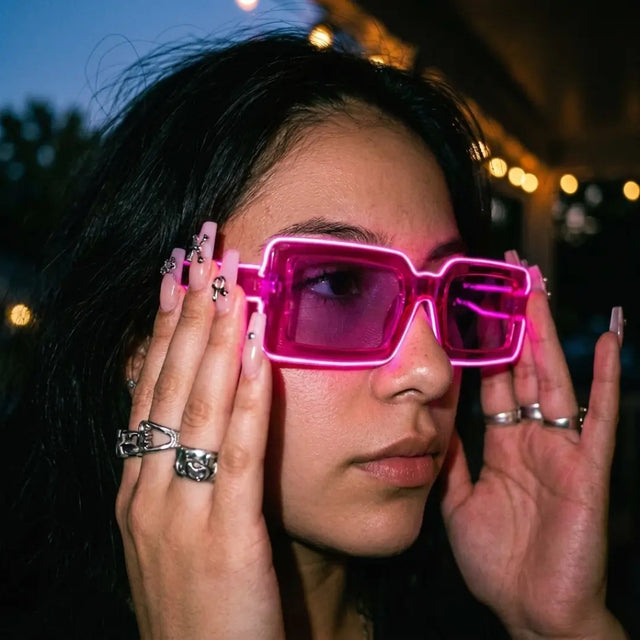 Woman at a night party lifting pink glowing LED light up party sunglasses with purple tinted lenses, futuristic cyberpunk led glasses and festival sunglasses for raves, EDM concerts, and glow parties, Neon Cowboys