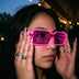 Woman at a night party lifting pink glowing LED light up party sunglasses with purple tinted lenses, futuristic cyberpunk led glasses and festival sunglasses for raves, EDM concerts, and glow parties, Neon Cowboys