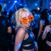 Blonde woman dancing at a rave in orange LED light up party sunglasses under blue stage lights, glowing futuristic party glasses and festival sunglasses for raves, EDM concerts, and Burning Man, Neon Cowboys