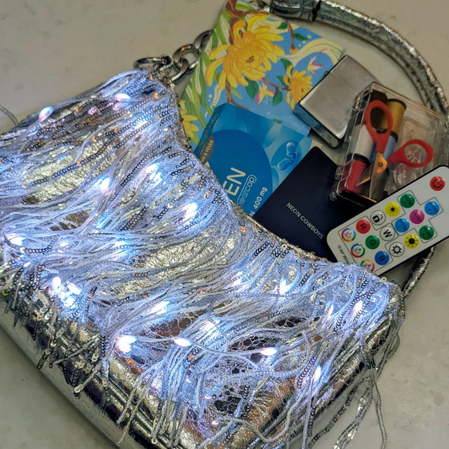 Open silver LED fringe purse glowing white showing its roomy interior and remote control, a light up purse and clear-bag concert alternative perfect for raves, music festivals, concerts and disco cowgirl nights out, Neon Cowboys