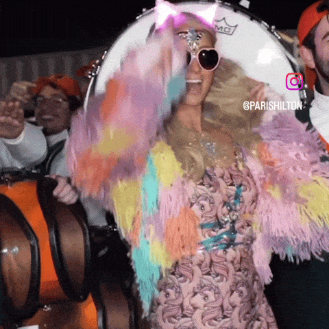 Paris Hilton with fluffy rainbow outfit wearing multiple LED rhinestone face gems - Complete festival look combining illuminated facial jewelry with colorful costume for EDM concerts, Pride parades, art installations, and immersive events