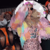 Paris Hilton with fluffy rainbow outfit wearing multiple LED rhinestone face gems - Complete festival look combining illuminated facial jewelry with colorful costume for EDM concerts, Pride parades, art installations, and immersive events
