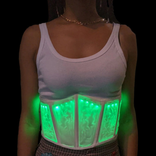 Front view of woman wearing bright green programmable LED corset with changing light patterns over white tank top, perfect for glow parties