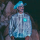 Male model wearing futuristic silver light-up horse jacket with glowing blue Neon Cowboys logo on front at nighttime music festival for cyberpunk rave fashion