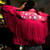 Animated Starlight Fringe Jacket, back of a pink fringe jacket showing glowing white and blue LED light-up stars at a dim bar, an led fringe jacket and light up jacket stagewear for rave performers, raves, EDM concerts and Pride, Neon Cowboys