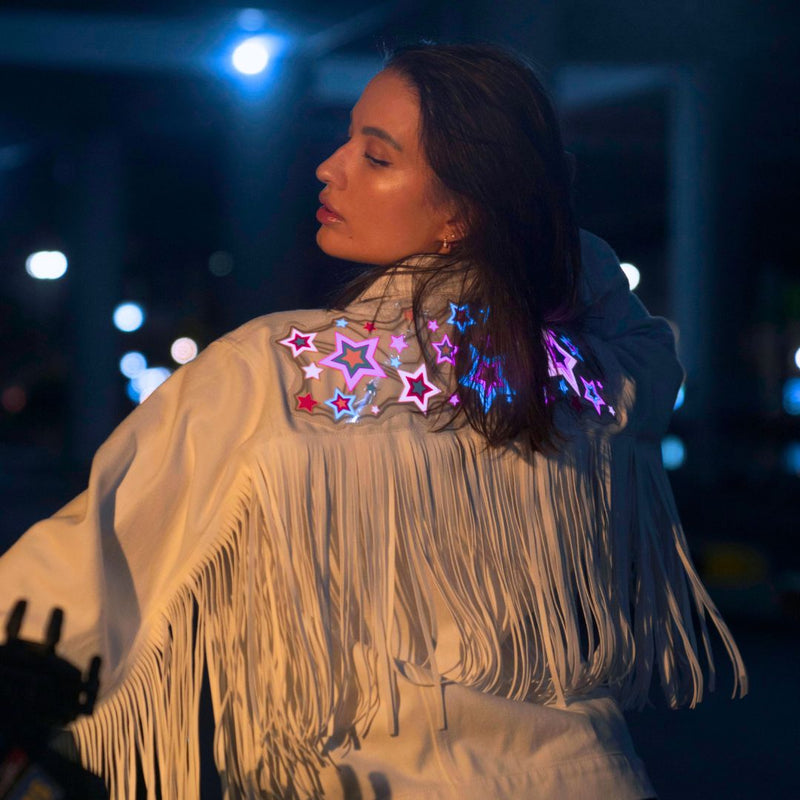 Animated Starlight Jacket with Fringe, woman in a white LED fringe jacket with glowing pink and blue light-up stars across the back at night, an led fringe jacket and light up jacket for go-go dancers, festival dancers and stagewear at raves, EDM concerts and Coachella, Neon Cowboys