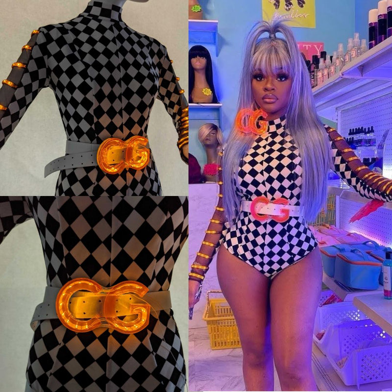 Performer in a checkered bodysuit wearing a custom Neon Cowboys light up CG belt buckle glowing orange with detail insets, as JT from City Girls styled it in a music video, a trending led festival fashion accessory for stage, concerts and raves, Neon Cowboys