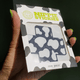 Hand holding open package of X-shaped nipple stickies displaying cow print design perfect for country concerts and western themed events