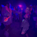 Group of women dancing in blacklight with glowing programmable LED corsets in vibrant colors at EDM festival, illuminating dance floor