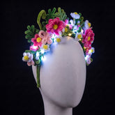 Floral pipe cleaner headband by Neon Cowboys on a white mannequin, a crown of handmade pink and white daisies and green fern leaves glowing with cool white LED fairy lights (included, you add them yourself), a light-up flower crown for festivals, raves, fairy and Halloween costumes