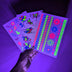 Hand holding glow-in-the-dark tattoo sheet under UV light - Illuminated temporary tattoos showing vibrant colors for nighttime events