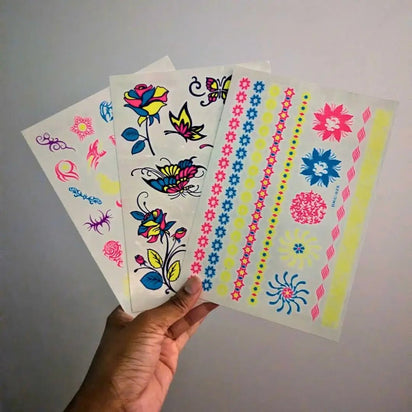 Hand holding glow-in-the-dark tattoo sheet in natural light - Temporary tattoo designs visible before UV activation for daytime wear