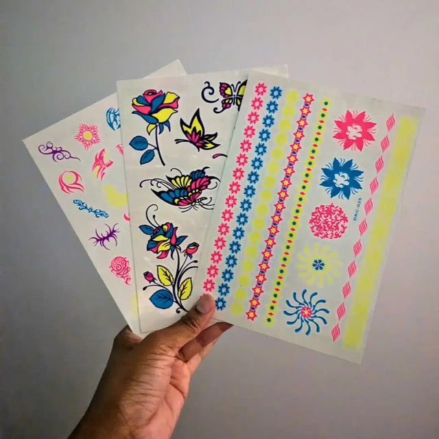 Hand holding glow-in-the-dark tattoo sheet in natural light - Temporary tattoo designs visible before UV activation for daytime wear