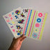 Hand holding glow-in-the-dark tattoo sheet in natural light - Temporary tattoo designs visible before UV activation for daytime wear