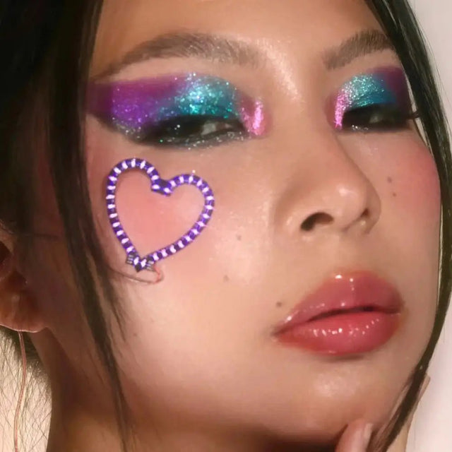 Woman with rainbow makeup and heart LED sticker - Colorful festival-ready look combining illuminated facial jewelry for Pride events, EDM festivals, artistic photoshoots, and theatrical performances