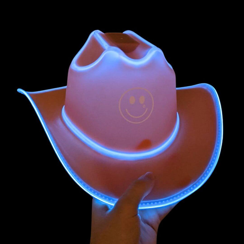 Hand holding a white light up cowboy hat with a smiley face and blue LED trim glowing brightly, Kacey Musgraves Golden Hour tour merchandise, a neon cowboy hat and glow cowboy hat for country concerts, music festivals and rave cowgirl outfits, Neon Cowboys